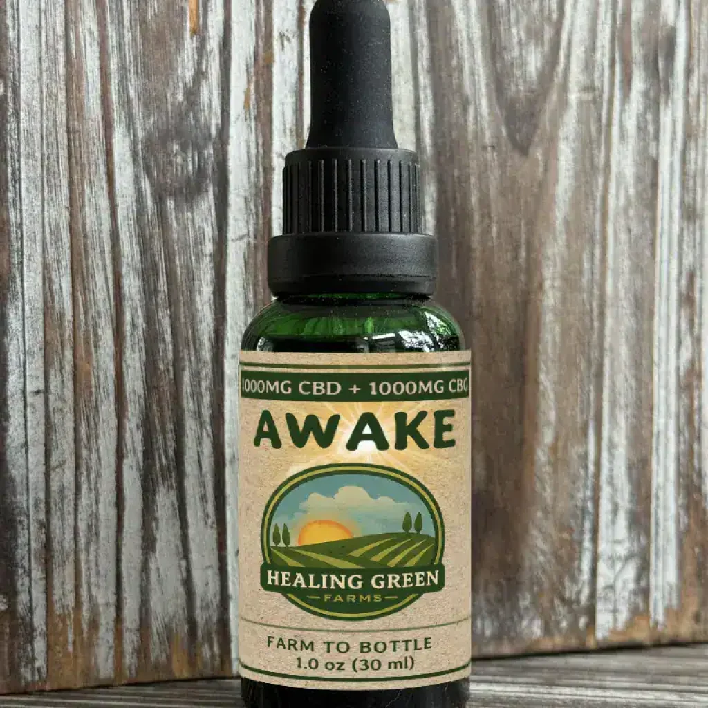 A green glass dropper bottle labeled "AWAKE & RELAX Combo" from Healing Green Farms, containing 1000mg CBD and 1000mg CBG, sits on rustic wood. Its label shows a sunrise over fields and reads "Farm to Bottle, 1.0 oz (30 ml).