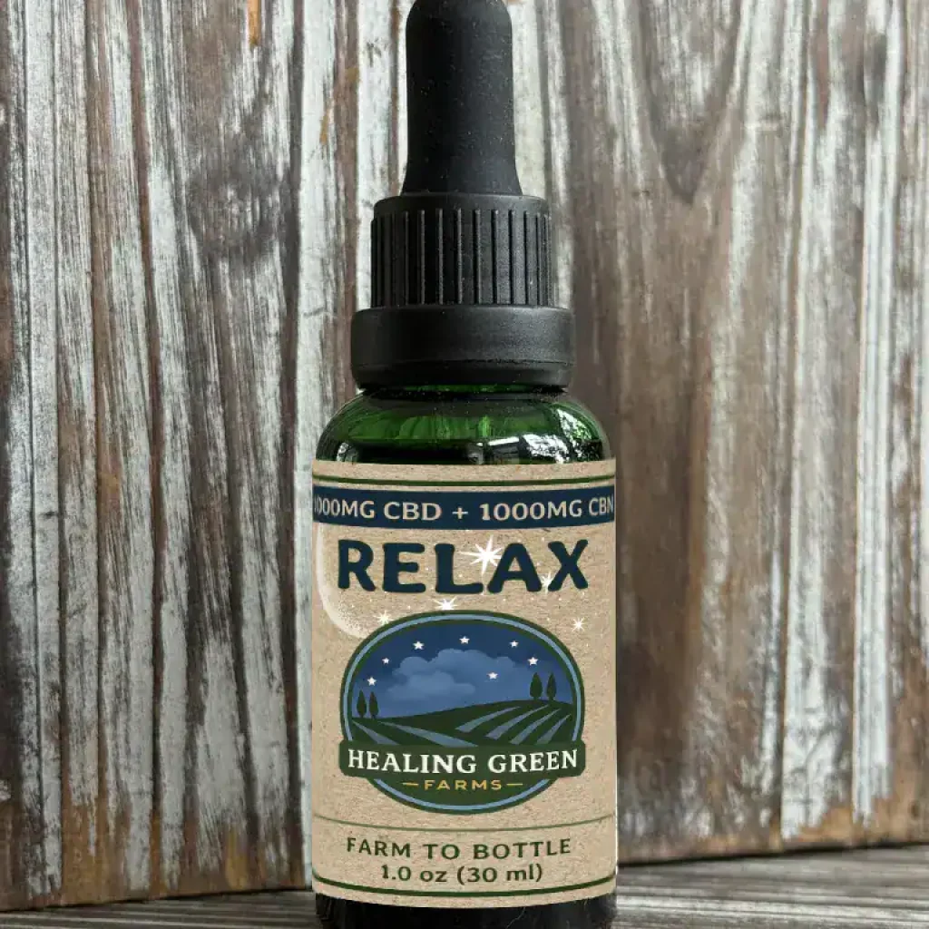 A green glass dropper bottle labeled "AWAKE & RELAX Combo" with 1000mg CBD + 1000mg CBN from Healing Green Farms sits on a wooden surface against a rustic wood background.