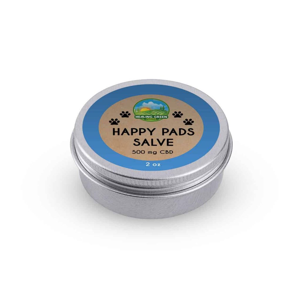 A round silver tin labeled "Happy Pads Skin Soothing Salve for Pets, 2 oz, 500 mg CBD" features a blue border with paw prints and a lid showing a mountain and green field logo.